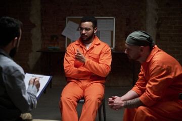 Group of young men participating in group therapy session in prison setting, therapist taking notes...