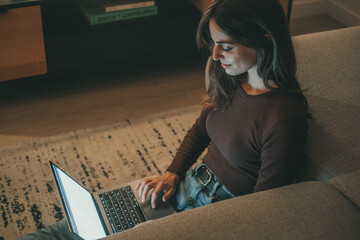 Young woman working late at home with warm lamp light – student or freelancer using laptop for...