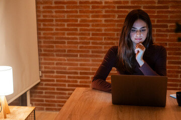 Young woman working late at home with warm lamp light – student or freelancer using laptop for...