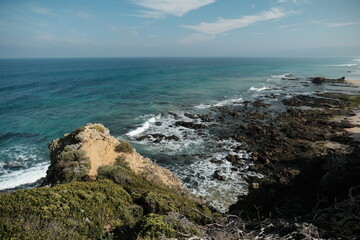 Dramatic rock coastline stretches out from Split Point Lookout towards the iconic Split Point Lighthouse under a vast sky. Rugged cliffs meet the crashing waves.