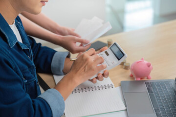 Calculating Finances. Young man using calculator for budgeting with piggy bank in view.