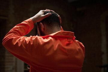 Caucasian man sitting with hands on head wearing prison uniform participating in group therapy...