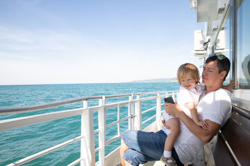 A man and a boy on a white boat in the sea are sitting by the side, father and son are enjoying a sea trip