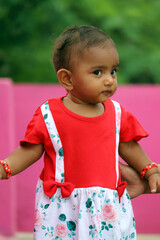 Adorable baby girl in a vibrant red and white floral dress posing outdoors
