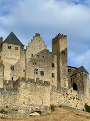 Medieval fortified city of Carcassonne, France. Stone fortification with imposing walls and conical towers under a moody sky. Steep slope covered with dry grass leads up to the structure