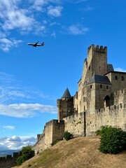 A plane flies over the medieval fortress of Carcassonne, France. The scene captures a moment where modern aviation intersects with historical grandeur. 