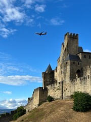 A plane flies over the medieval fortress of Carcassonne, France. The scene captures a moment where modern aviation intersects with historical grandeur. 
