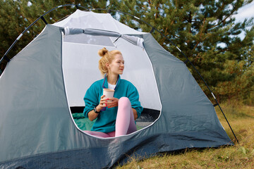 Woman enjoying coffee while relaxing in a tent during a peaceful camping morning