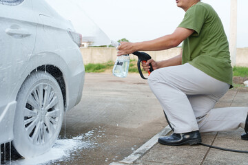 A smiling man is washing his car with soapy water under bright sunlight, showing his enthusiasm and joy in his daily work.