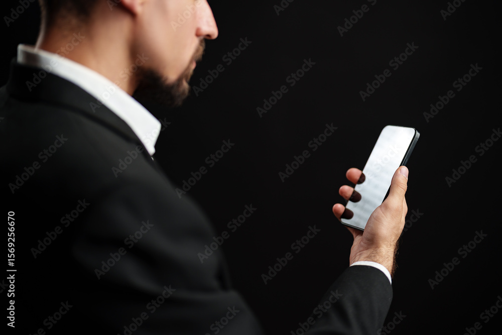 Aufkleber man in formal attire checking smartphone against a dark background in a modern setting