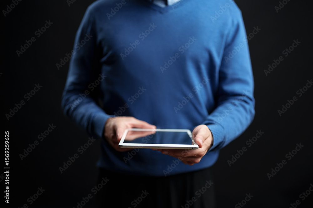 Poster person using a tablet while standing against a dark background during an indoor setting in a casual 