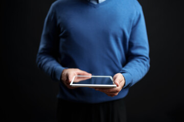 Person using a tablet while standing against a dark background during an indoor setting in a casual environment