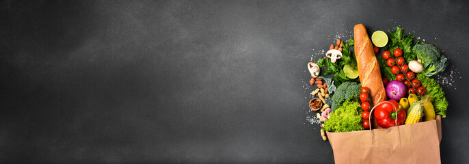 Food background. Wide banner with paper bag filled with fresh vegetables, fruits and various...