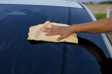 A smiling man is washing his car with soapy water under bright sunlight, showing his enthusiasm and joy in his daily work.