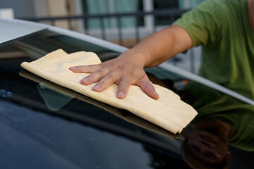 A smiling man is washing his car with soapy water under bright sunlight, showing his enthusiasm and joy in his daily work.