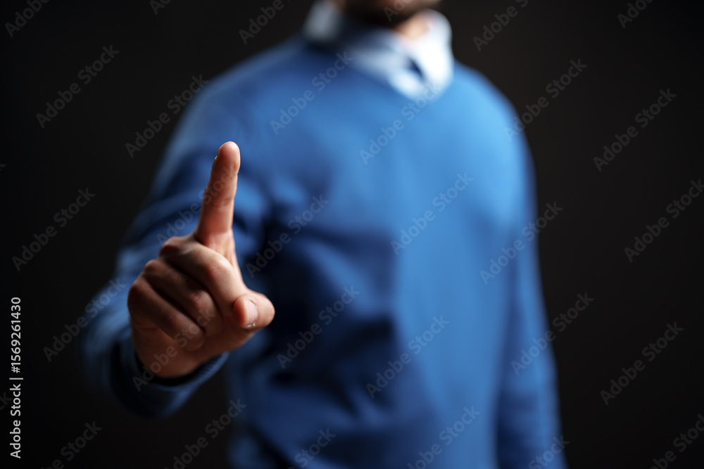 Poster man signaling to pause with one finger raised, dressed in casual attire against a dark background wi