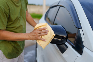 A smiling man is washing his car with soapy water under bright sunlight, showing his enthusiasm and joy in his daily work.