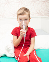 Sad little boy sitting in red t-shirt and almost crying, breathing nebulizer