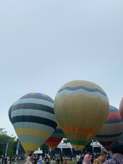 Colorful hot air balloons festival display distinct horizontal stripes are being inflated on the cloudy sky provide  backdrop. 