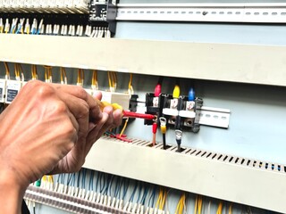 Electrician hands using insulated screwdriver to adjust circuit in industrial control panel. High voltage maintenance and electrical engineering concept in fact