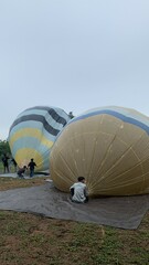 Colorful hot air balloons festival display distinct horizontal stripes are being inflated on the cloudy sky provide  backdrop. 