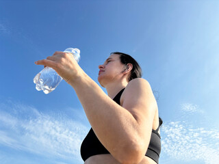  Sporty woman holding water bottle against blue sky, outdoor fitness and active healthy lifestyle...