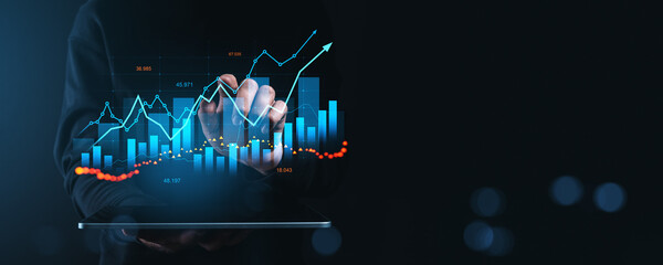 Businessman analyzing financial data on futuristic digital screen with graphs and charts on a dark...