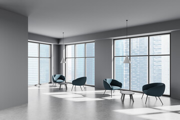 Modern office interior with blue armchairs and pendant lights in front of large glass windows...