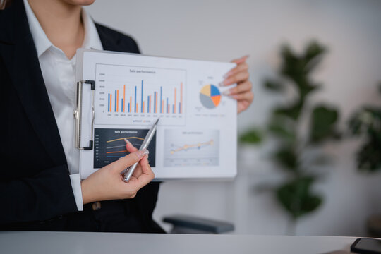 Businesswoman using pen pointing financial chart and graph document presenting sales performance report during meeting with colleague in office