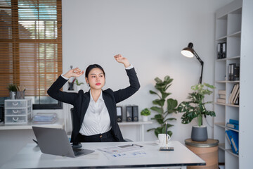 Young businesswoman is stretching her arms while sitting at her desk in a modern office after...