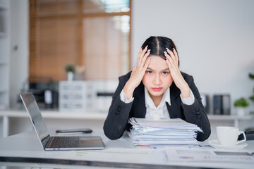 Young Asian businesswoman is having a headache and feeling tired from working on a laptop at the...