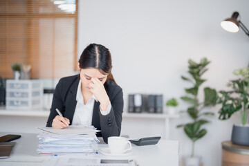 Young Asian businesswoman experiencing a headache, massaging her temples while managing a laptop...