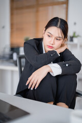 Young Asian businesswoman is sitting at desk and feeling stressed and tired while working on laptop...