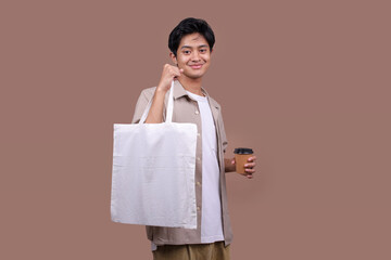Asian Man Carrying Blank Totebag and Takeaway Coffee Cup on Beige Studio