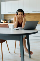 Young woman in pajamas making call using laptop in kitchen in morning