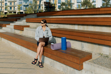 Young female instructor sitting on bench with laptop and equipment for training