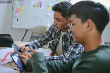 Two Young Men Looking At Smartphone Reviewing Content On His Mobile Phone During Study Session