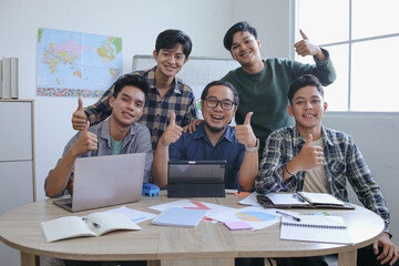 Group Of College Students With Teacher Giving Thumbs Up And Posing Confidently At Round Office Table