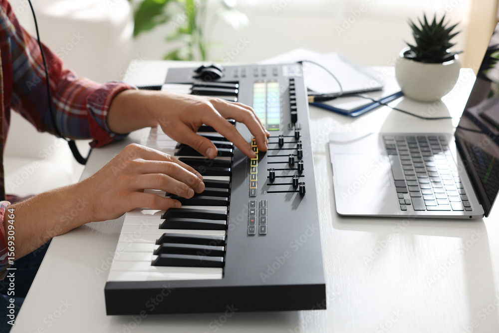 Poster man working with midi keyboard at white table indoors, closeup