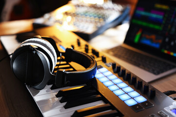 MIDI keyboard with headphones, laptop and dj mixer on wooden table indoors, closeup