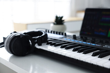 MIDI keyboard, headphones and laptop on white wooden table indoors, closeup