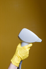 Hand in disposable glove holding professional laser hair removal handle on yellow background. Copy...