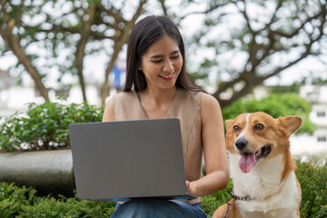 Remote Work and Pet Companionship. Young woman smiling while working on laptop with her corgi dog.