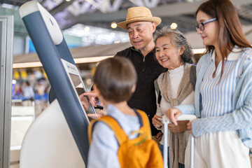 Asian family using airport self check-in kiosk together, multigenerational group interacting with...