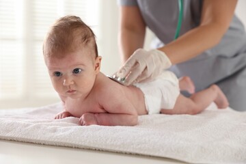 Pediatrician examining baby with stethoscope at table in clinic, closeup