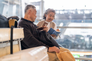 Senior asian couple sitting with luggage checking passport planning trip showing travel preparation...