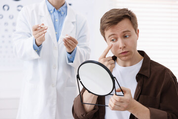 Young man putting on contact lenses near mirror in ophthalmologist office