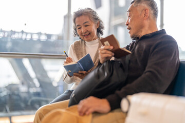 Senior asian couple sitting with luggage checking passport planning trip showing travel preparation...