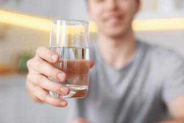 Man with glass of water in kitchen, selective focus