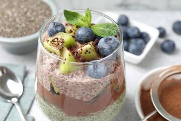 Delicious chocolate pudding with chia seeds, kiwi, mint and blueberries in glass on grey table,...